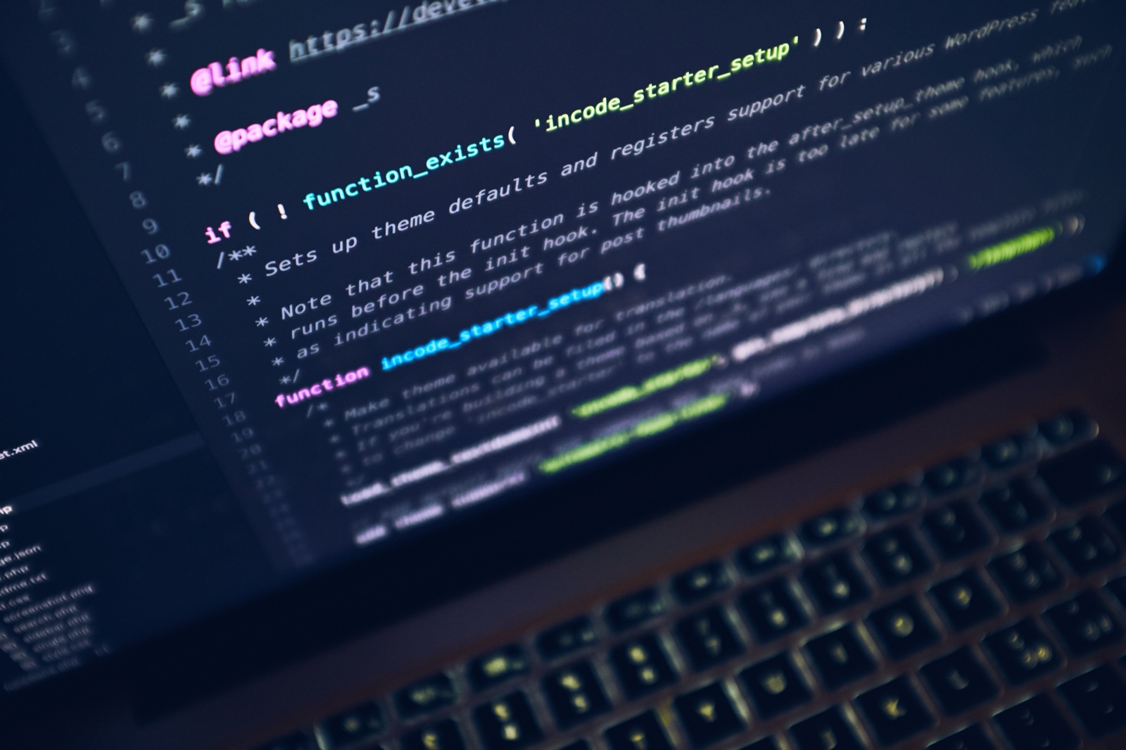 A laptop screen full of colorful code in a dark editor, shot at an angle with the backlit keyboard blurred below.